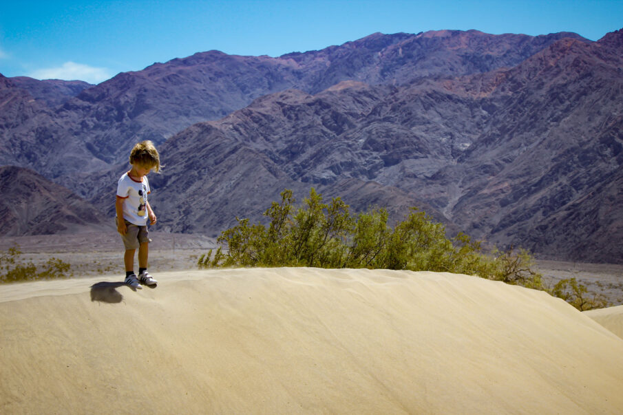 A child stands atop the sand dune at Mesquite Flats Sand Dunes in Death Valley National Park